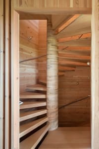 A modern, spiral staircase with wooden steps and railings inside a wooden building.