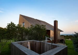An image of a modern residential building with a wooden exterior, featuring a square hot tub with water cascading into it.