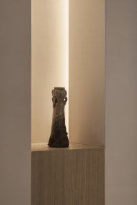 A ceramic vase with an industrial style design sits on a wooden pedestal in a minimalist setting.