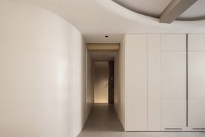 A modern minimalist corridor featuring white concrete walls, a metal shelf, and a door leading to a residential area.