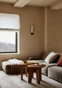 A modern minimalist living room with fabric furniture and wall sconce.