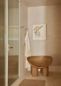 A modern bathroom featuring a minimalistic and organic design with concrete materials and an unusual chair.