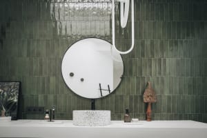 A modern bathroom with green ceramic tiles, a round mirror, and a white vessel sink.