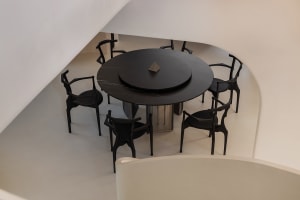 A modern dining room featuring a round black marble table with a central black marble plate, surrounded by black metal chairs