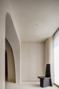 A modern minimalist bedroom with a concrete floor and wall, featuring sleek, clean lines and a unique black chair.