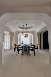 A minimalist dining room with round concrete floor, black chairs, a round table, and abstract lighting fixtures.