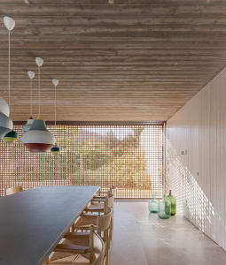 A modern minimalist dining room with a long wooden table and chairs, featuring colorful pendant lights and a lattice window.