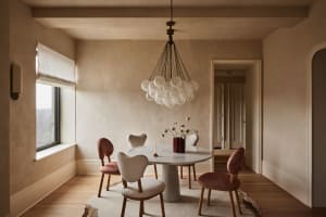 A modern dining room with a marble table, upholstered chairs, and a chandelier with frosted glass globes.