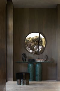A modern interior space featuring a console table with a green marble base and a small round mirrored wall decoration.
