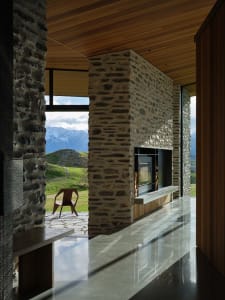 Modern minimalist living room with stone fireplace and floor-to-ceiling windows overlooking mountains and hills.