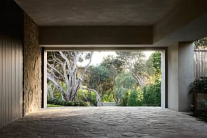 A modern mansion exterior with stone and concrete walls, featuring a large courtyard and surrounding trees.