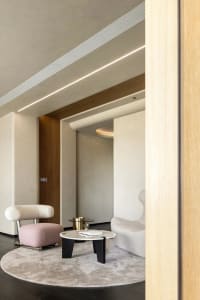Modern living room with white concrete walls, wood paneling, and a round rug with a coffee table and a pink cushioned chair.