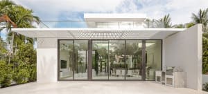 Modern outdoor kitchen with concrete patio and white accents, featuring a grill and seating area with hanging fan.
