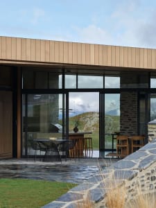 Modern residential interior featuring large glass windows, stone walls, and wooden elements.