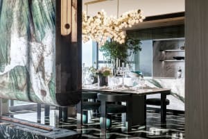 A modern dining room featuring a marble table and floor. Decorative elements include a floral centerpiece and a chandelier.