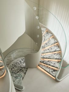 A modern, spiral staircase with marble steps and a glass handrail.