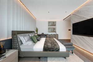 A minimalist bedroom with a modern design, featuring a large bed, white walls, and a marble-like accent wall.