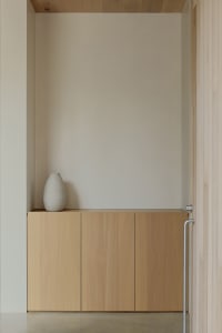 A minimalist sideboard made of natural wood with a single white vase on top.