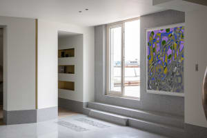 A modern living room with concrete flooring, large windows, and abstract art.