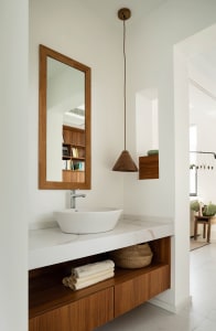 Modern minimalist bathroom with a white marble sink, wooden shelves, and a wooden pendant light.