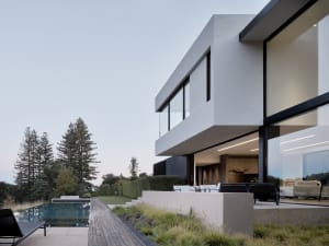 A modern house with a concrete exterior features expansive glass windows and a sleek design.