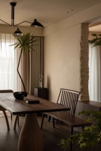 A minimalist dining room with a wooden table, stone pillars, and modern lighting fixtures.