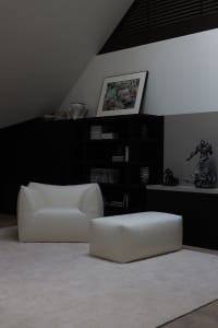 A modern living room with a white leather armchair and footstool, black furniture and decor, and minimalist design.