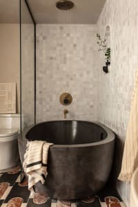 A modern bathroom with a black concrete bathtub, white tile walls, and a glass shower enclosure.