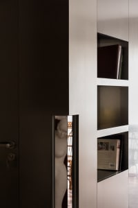 A modern interior design featuring wooden bookshelves filled with books and a sculpture peeking from behind a wall.