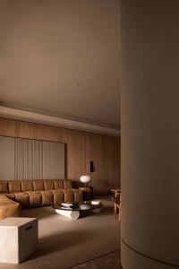 A modern minimalist living room with brown leather furniture, wooden paneling, and marble accents.