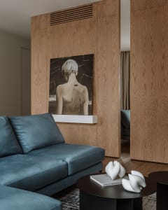 A modern living room with a blue sofa, wooden walls, and a white abstract painting of a person's back.