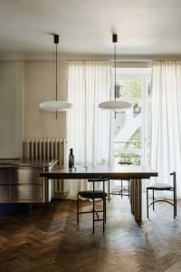 A modern minimalist dining room featuring a wooden table, glass pendant lights, and metallic chairs.
