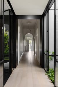 A modern minimalist hallway with light-colored wooden floors, clear glass panels, and white walls.
