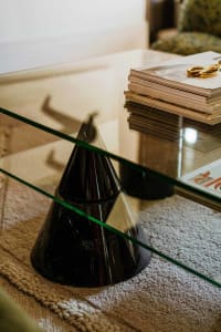 A glass pyramid-shaped vase on a glass coffee table with books and a pair of scissors on top.