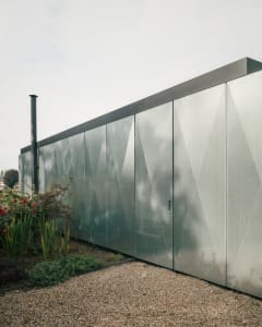 A modern exterior house with a metallic facade, featuring geometric patterns and a chimney.
