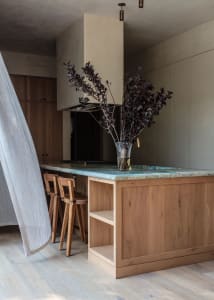 Modern kitchen interior with wooden cabinets, marble countertop, and a vase of purple leaf branches