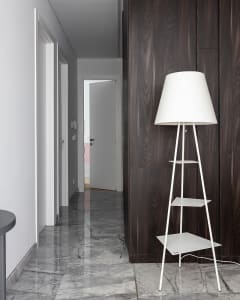 Modern minimalist interior featuring a white floor lamp with three shelves and a black wooden wall paneling.