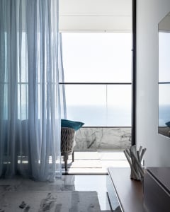 Modern residential space featuring glass, marble, and upholstered furniture with a view of the sea.