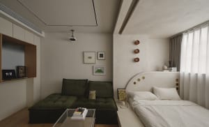 A minimalist bedroom featuring a green upholstered couch, a white bed with a curved headboard, framed art on the wall, and a 