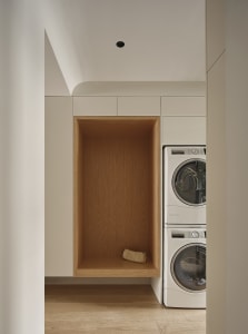 A modern laundry room featuring wooden cabinets, a washing machine, and a small pouch on a shelf.
