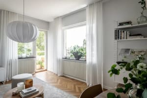 Modern living room featuring white wooden furniture, light gray cotton curtains, and a round wooden table with books, candles