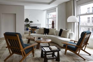 A modern living room featuring a curved white sofa, blue upholstered chairs, and a wooden coffee table with books and candles