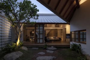 A modern residential outdoor space featuring a wooden deck with furniture, a concrete wall, and a glass roof.
