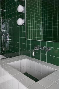 A modern bathroom with green-tiled walls, a white sink, and chrome fixtures.