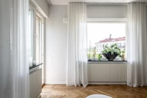 A modern living room with transparent curtains, wooden flooring, and a large window.