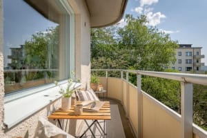 Outdoor balcony with wooden furniture, concrete floor, and greenery.