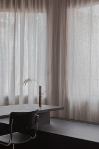 Minimalist room with transparent curtains, wooden table, and black chair