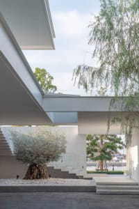An indoor staircase with a concrete base surrounded by a gravel patio, leading to a green area with trees and a light blue sk