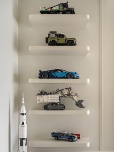 Five white floating shelves displaying various toy vehicles and a model rocket.