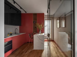 A modern kitchen featuring red cabinets, white marble top, and wooden flooring.
